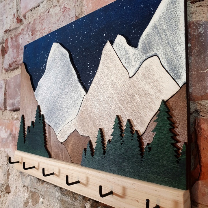 Ručne maľovaný drevený vešiak na kľúče s motívom hôr, 28 × 20 cm, 6 háčikov. Vešiak na kľúče s horským motívom poskytne zväzkom pripravené miesto a zároveň doplní predsieň maľovanou dekoráciou. Šesť čiernych háčikov umožní rozdeliť kľúče podľa používania.